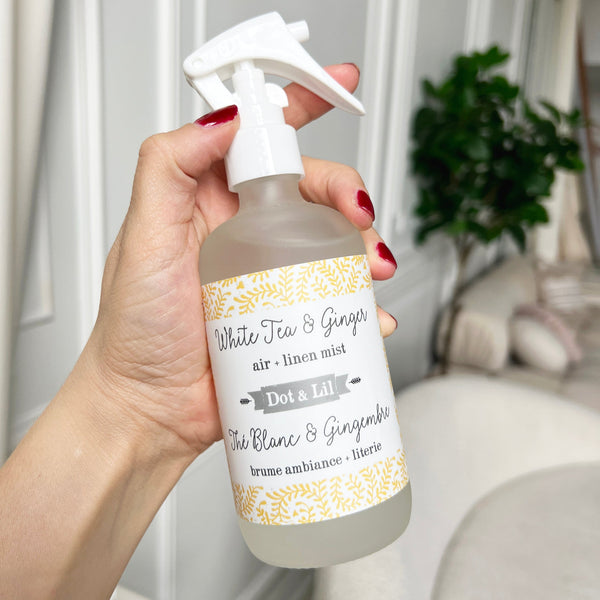 Hand holding a bottle of 'White Tea & Ginger' air linen mist with a decorative label.